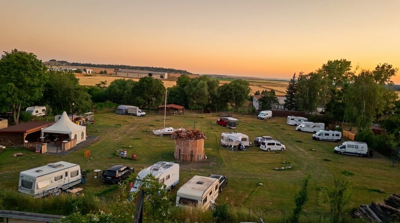 Der Campingplatz Auf der Hohe im Abendlicht, vom Hotel aus gesehen: Wohnmobile und Wohnwagen auf der Wiese, dahinter die Felder des Vorharzes