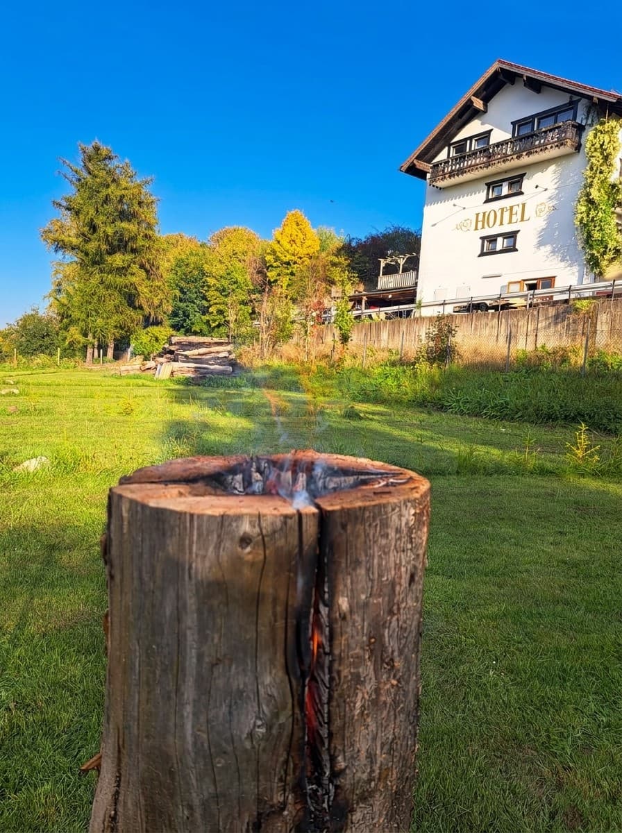 Brennendes Schwedenfeuer auf der Wiese in der Sonne, im Hintergrund das weiße Hotel mit Holzbalkon
